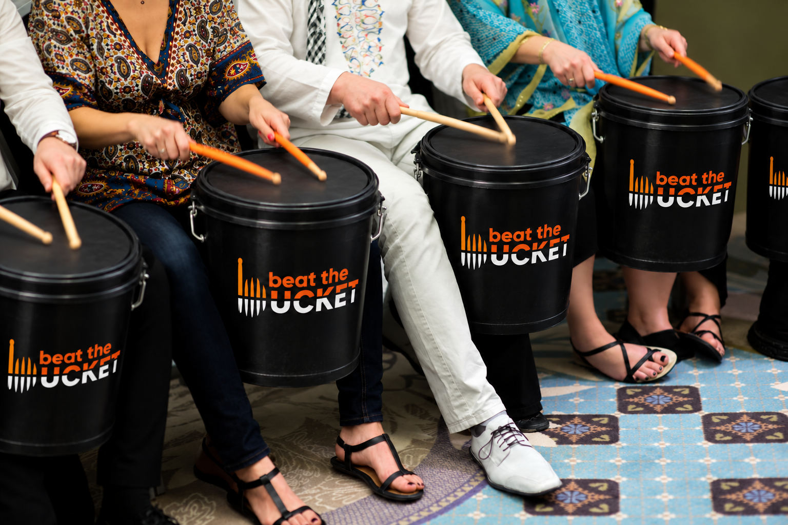 A group using drumsticks on branded black buckets together.